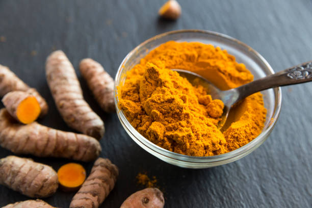 glass bowl of curcuma powder and fresh organic curcuma on slate - turmeric stock pictures, royalty-free photos & images