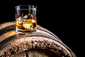 Glass of whisky with ice on old wooden barrel