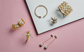 golden bracelets and earrings with pearls on pink and white background