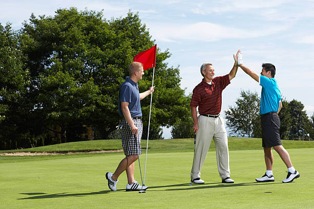 golfers high fiving on putting green standing next to golfer holding flag - golfeur photos et images de collection