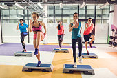 Group of athletic people exercising step aerobics in a gym.