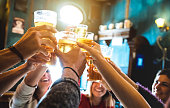 Group of happy friends drinking and toasting beer at brewery bar restaurant - Friendship concept with young people having fun together at cool vintage pub - Focus on middle pint glass - High iso image