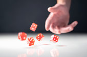Hand throwing and rolling dice. Gambler tossing five red poker and casino dice on table. Man gambling or playing board game.