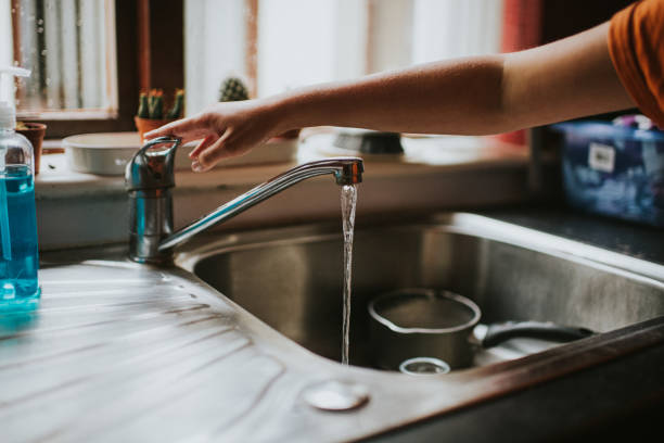 hand turning off a running chrome tap in a kitchen - ralo - fotografias e filmes do acervo