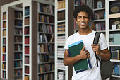 Handsome afro student posing on bookshelves background