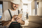 Happy construction worker using cell phone during home renovation.