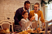 Happy Jewish family lightning the menorah before a meal at dining table.