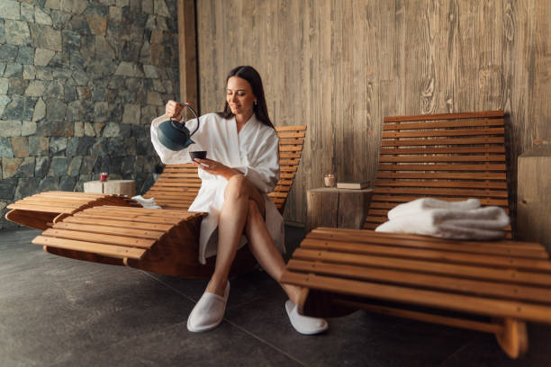 happy mid adult woman with bathrobe sitting in wellness resort, relaxing. - spa stock pictures, royalty-free photos & images