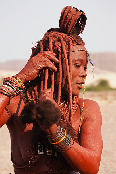 a himba girl mixes ochre and fat to apply to her exposed skin and hair - the himba peple stock pictures, royalty-free photos & images