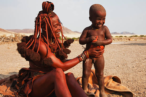 a himba woman mixes ochre and fat to apply to exposed skin and hair for beauty and sun protection - the himba peple stock pictures, royalty-free photos & images