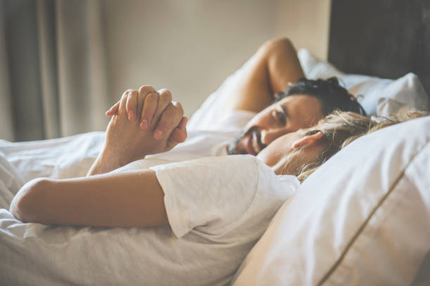 hispanic couple holding hands in bed - happy couple on bed stock pictures, royalty-free photos & images