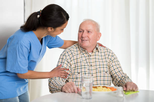 home caregiver giving senior man lunch -  senior care aide stock pictures, royalty-free photos & images