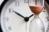 Hourglass on the background of office watch as time passing concept for business deadline, urgency and running out of time. Sand clock, business time management concept