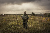 Hunter with hunting ammunition gun going through rural field during hunting season in overcast day