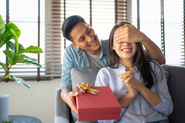 image of young guy with giftbox closing his girlfriend eyes to make a surprise for her. - man surprised girl stock pictures, royalty-free photos & images