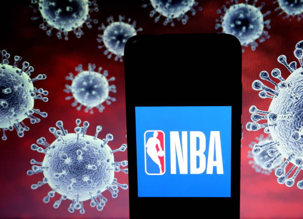 In this photo illustration a National Basketball Association logo seen displayed on a smartphone with a computer model of the COVID19 coronavirus in...