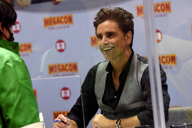 john stamos behind a plexiglas shield interacts with fans at megacon picture