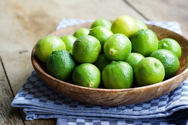 key limes, citrus aurantiifolia, in a wooden bowl - key lime stock pictures, royalty-free photos & images