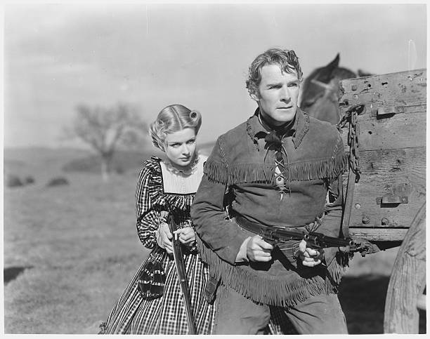 Kirk Jordan and Ivy Preston stand alongside a wagon, brandishing guns in a scene from the 1938 western, The Texans.