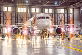 Large-scale inspection of all aircraft systems in the aircraft hangar by worker mechanics and other specialists. Bright light outside the garage door.