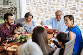 Latin senior man serving the food to his family at dinner table