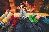 Legs view of happy family wearing warm socks in front of fireplace - Winter, love and cozy concept - Focus on center grey woolen socks
