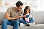 Little girl and dad saving money in piggy bank