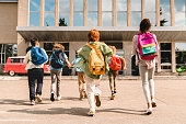 Little kids schoolchildren pupils students running hurrying to the school building for classes lessons from to the school bus. Welcome back to school. The new academic semester year start