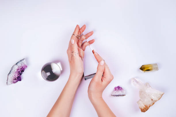 magic set for rituals. hands with nude pink manicure and many rings on fingers are holding glass pyramid near magic crystal ball, crystals and esoteric tools on white background. flat lay style with copy space for your design - astrologia - fotografias e filmes do acervo