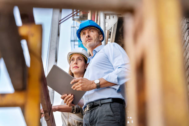 male architect holding digital tablet while examining construction site with coworker - construction wifi stock pictures, royalty-free photos & images