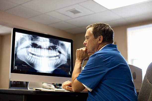 male dentist viewing x-ray on computer screen. - dentistas  - fotografias e filmes do acervo