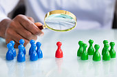 Male Looking At Colorful Pawns With Magnifying Glass