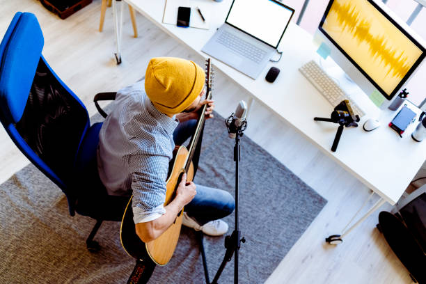 male vlogger playing guitar while live streaming on camera at recording studio - streaming live - fotografias e filmes do acervo