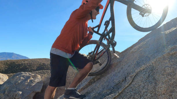 Man carries mountain bike up boulder in desert
