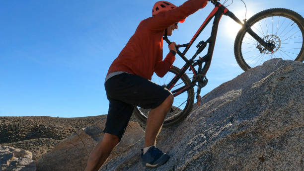 Man carries mountain bike up boulder in desert
