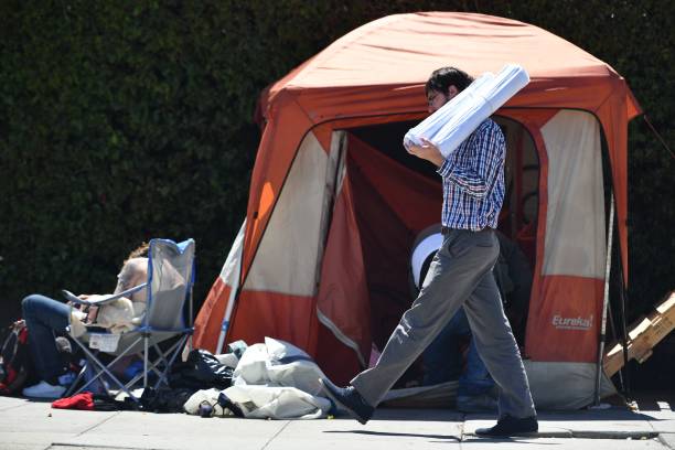 Man carrying blueprints passes a homeless encampment in downtown San Francisco, California on June 2016. Homelessness is on the rise in the city...