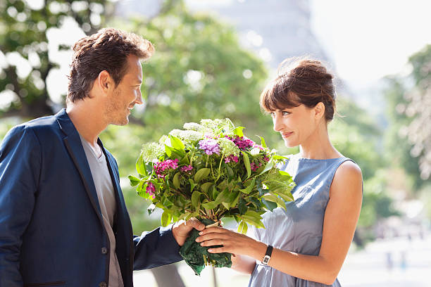 man giving a bouquet of flowers to a woman with the eiffel tower in the background, paris, ile-de-france, france - husband giving wife flowers stock pictures, royalty-free photos & images