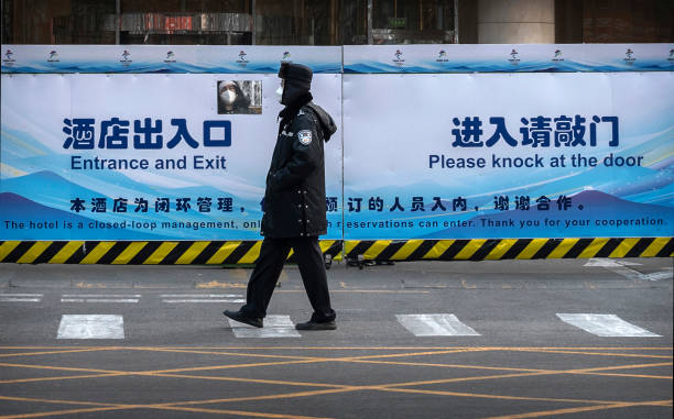 Man looks through a window in a fence as a security guard walks in front of a fenced in hotel being used as part of the closed loop management for...