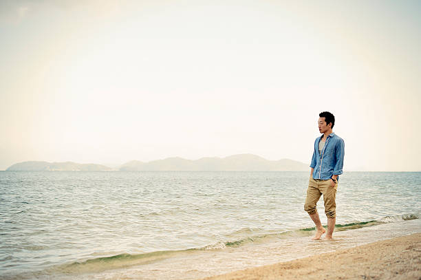 man walking on the beach - asian man in the beach stock pictures, royalty-free photos & images