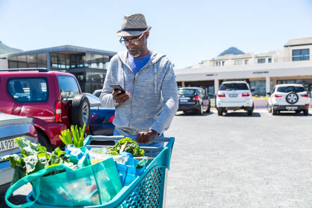 mature african man pushing shopping cart while looking at smart phone picture