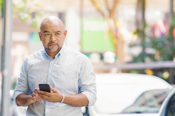 mature confused asian man mobile phone in hand looking lost - asian bald guy stock pictures, royalty-free photos & images