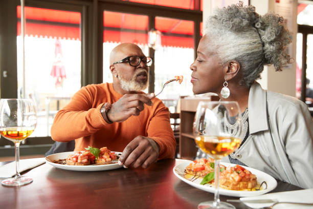 mature man feeding woman while sitting at restaurant picture