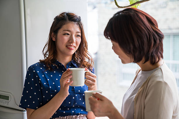 mid adult daughter and senior mother talking while having coffee - two asian middle-aged woman stock pictures, royalty-free photos & images