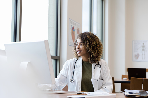 Mid adult female doctor reviews patient records on desktop PC
