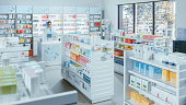 Modern Pharmacy Drugstore with Shelves full of Packages Full of Modern Medicine, Drugs, Vitamin Boxes, Supplements. In Background Professional Pharmacist Working at Checkout Counter.