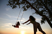 Mom pushes Daughter on swing set playing at sunset  silhouette