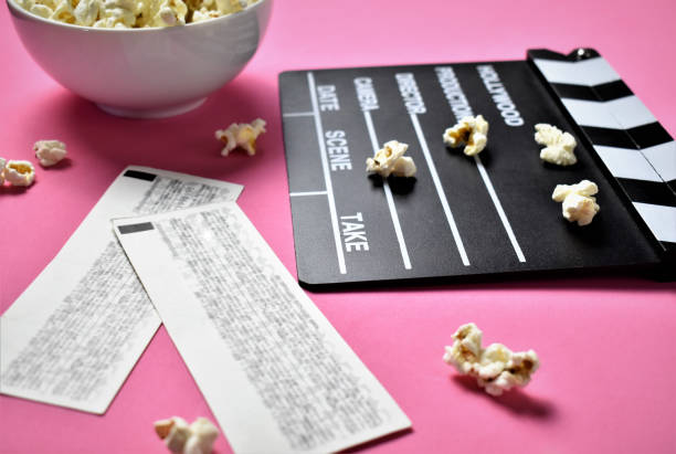 Movie clapper, movie tickets and popcorn on pink background