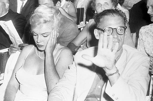 Movie queen Marilyn Monroe wears a bored expression as her playwright-husband Arthur Miller shoos photographers away at the Boston Arts Center...