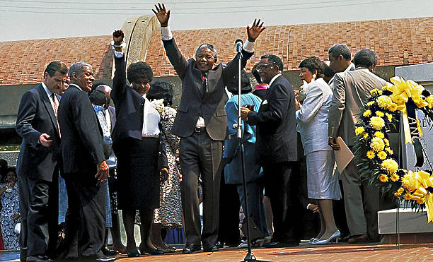 Nelson Mandela raises his hands in praise at the memorial of Martin Luther King Jr. Present are his former wife, Jesse Helms, SCLC president Joseph...