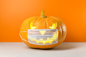 New normal concept. Glowing Halloween pumpkin in a protective medical mask on a orange background.